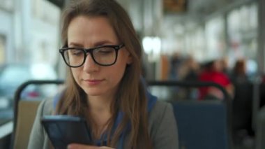 Toplu taşıma. Tramvayda gözlüklü bir kadın akıllı telefon sohbeti yapıyor ve arkadaşlarıyla mesajlaşıyor. Şehir, şehir, ulaşım.