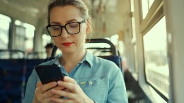 Public transport. Slow motion of woman in glasses in tram using smartphone chatting and texting with friends. City, urban, transportation.