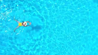 Top down view of a woman in yellow swimsuit swimming in the pool. Summer lifestyle