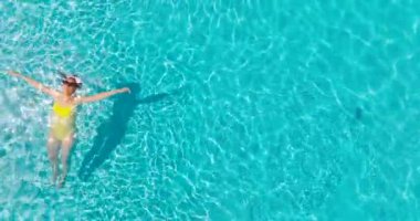 Sarı mayolu bir kadının havuzda sırt üstü yatışı. Kamera yavaşça yükselir ve saat yönünün tersine döner. Rahatlatıcı konsept, yaz yaşam tarzı