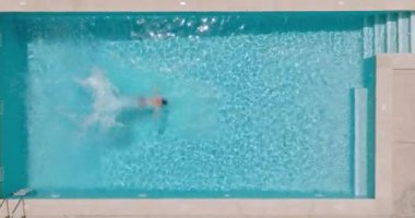 Top down view as a man dives into the pool and swims. Slow motion
