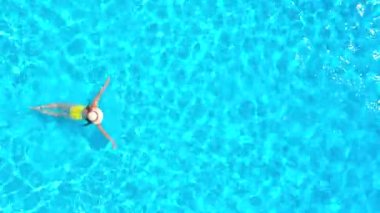 Top down view of a woman in yellow swimsuit swimming in the pool. Summer lifestyle