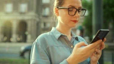 Woman using smartphone while standing outdoors at sunset. Communication, work day, busy life concept.