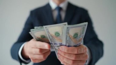 Resmi olarak giyinmiş bir adam Amerikan dolarlarını sayıyor, yakın plan. Yatırım, başarı, finansal beklentiler veya kariyer ilerlemesi kavramı.