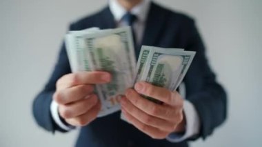 Resmi olarak giyinmiş bir adam Amerikan dolarlarını sayıyor, yakın plan. Yatırım, başarı, finansal beklentiler veya kariyer ilerlemesi kavramı.