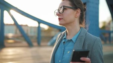 Sabahın erken saatlerinde şehirde dolaşan ve akıllı telefon kullanan beyaz bir iş kadını. Ağır çekim. İletişim, iş günü, yoğun yaşam konsepti.