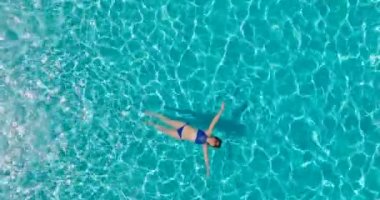 Top down view of a woman in a blue swimsuit lying on her back in the pool. Relaxing concept, summer lifestyle