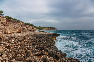 Kasvetli ve dramatik bir gökyüzünün altındaki Rocky sahili. Mallorca Adası, İspanya Akdeniz, Balear Adaları.
