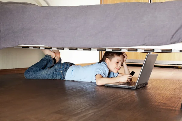 Niño con portátil y teléfono debajo de la cama —  Fotos de Stock