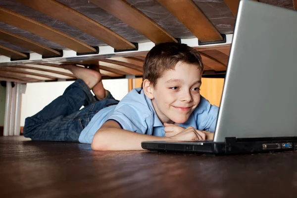 Criança jogando laptop sob a cama — Fotografia de Stock