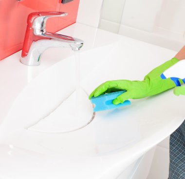 Kadın lavabo ve musluğu temizliyor.