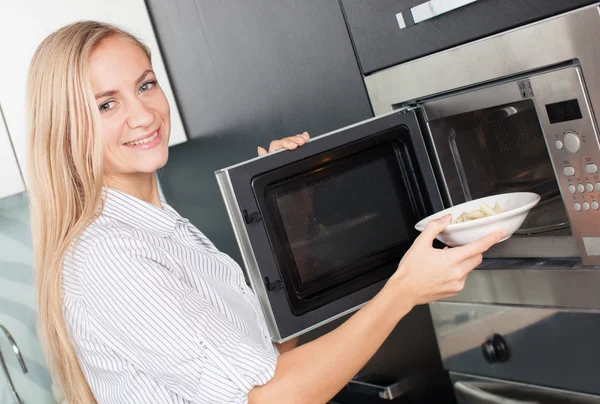 Kobieta rozgrzewa jedzenie w kuchence mikrofalowej — Zdjęcie stockowe