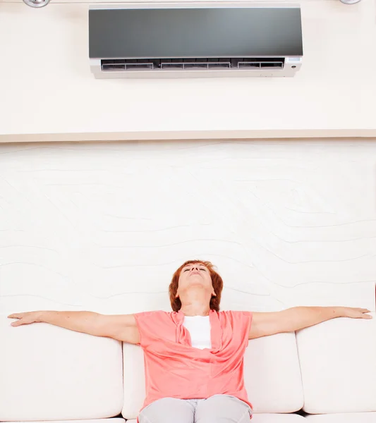 Woman escapes from the heat under the air conditioner — Stock Photo, Image