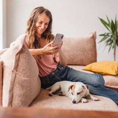 Gülümseyen kadın rahat ol ve cep telefonunu tut. İnternetten akıllı telefon kullanarak alışveriş yapmak. Çekici, mutlu, köpekli bir kadın.