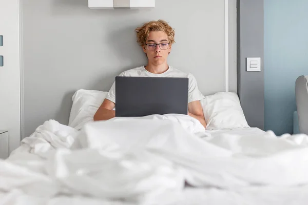 티셔츠를 침실에서 시간을 보내며 천으로된 담요를 침대에 노트북 컴퓨터를 만지고 — 스톡 사진