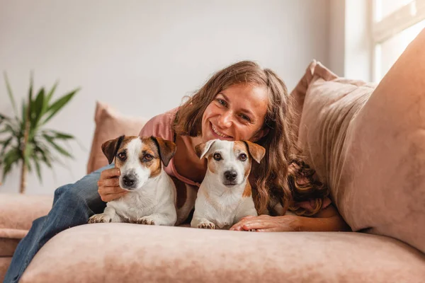 犬と一緒に幸せな女の子はソファの上の自宅で休んでいます 笑顔女性とともにペットオンソファ — ストック写真