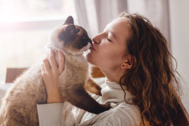 Ev sahiplerinin elinde sevimli bir kedi. Genç kız evcil hayvanını öpüyor. Kediyle oynayan kadın