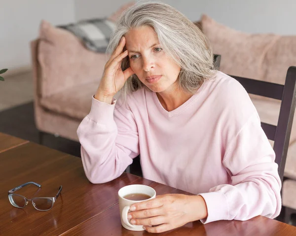 忧心忡忡的成熟女人坐在家里的客厅里 一个灰白头发的中年妇女 — 图库照片