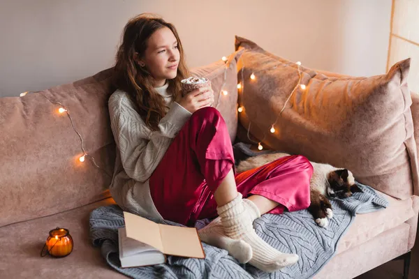 寒い秋や冬の週末猫の暖かいココアやマシュマロとコーヒーを飲む若い女性 ソファの上の編んだ靴下に怠惰な日 コスプレシーン 居心地の良いホームコンセプト — ストック写真