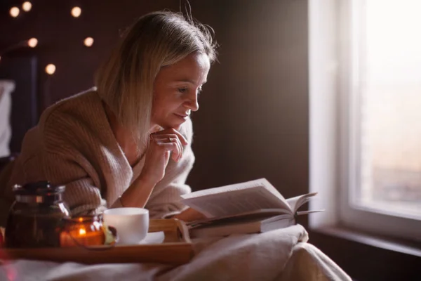 40多岁的成年女子在舒适的家中躺在床上看书 中年妇女在冬天或秋天的一天都会在卧室里休息 — 图库照片