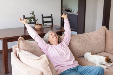 Orta yaşlı mutlu bir kadının portresi. Evdeki rahat koltukta dinleniyor. Gülümseyen, 50 'li yaşlarda yaşlı, kır saçlı, köpekli bir kadın.