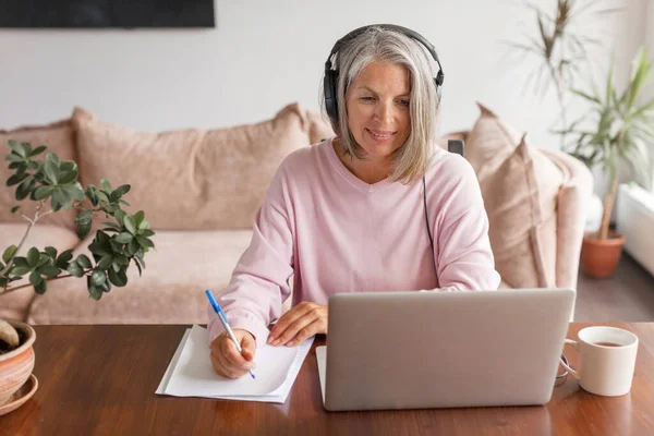 Χαμογελώντας Ώριμη Γυναίκα Φορώντας Ακουστικά Χρησιμοποιώντας Φορητό Υπολογιστή Στο Σπίτι — Φωτογραφία Αρχείου