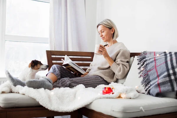 幸せな女性が居間で手に本を持っている 大人の女性は自宅でソファに座って 平日にリラックス — ストック写真