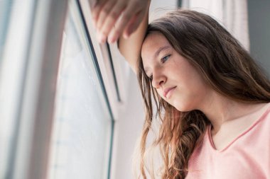 Sad pensive young woman at home Winter depression - seasonal affective disorder mental health looking out the window alone. Self isolation