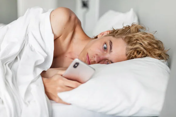 令人惊讶和担忧的是 男人躺在床上看着手机 却在等电话 可悲的少年读了坏的新东西 — 图库照片