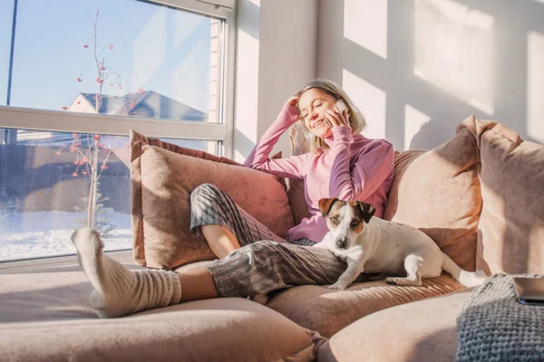 リビングルームでソファに座っている彼女の犬と中年の女性 冬の日に家で女性の電話 — ストック写真