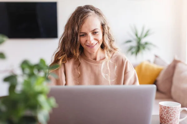 自宅のノートパソコンで働く幸せなカジュアルな美しい女性 笑顔のフリーランサー女性はコンピュータを見て — ストック写真