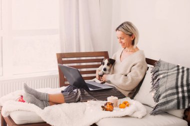 Çekici orta yaşlı hizmetçi kadın rahat koltukta oturuyor yetişkin kadın kahve içiyor bilgisayarlara bakıyor uzaktan kumandalı iş evde karantina altında hafta sonu oturma odasında kalıyor.