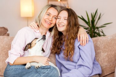 Gülümseyen beyaz bir anne. Kanepede oturup genç kız sohbeti yapıyor ve konuşuyor. Mutlu bir anne, genç bir kızla kanepede dinlenir, birlikte güzel bir hafta sonu geçiririz.