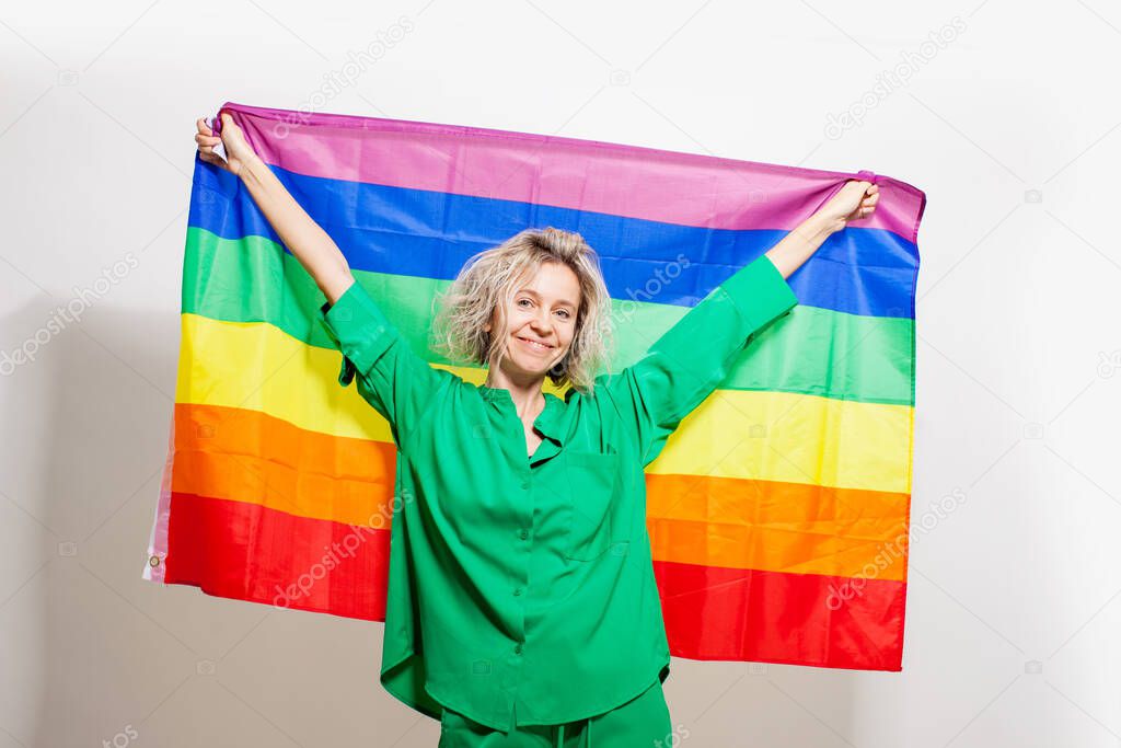 Cheerful beautiful middle aged woman smiling posing with rainbow LGBT flag celebrate parade show tolerance same marriages. Adult female isolated on white studio background indoors