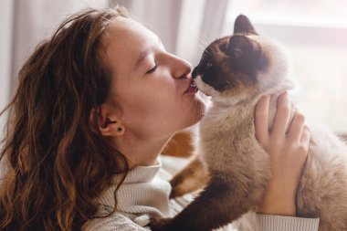 Mutlu genç kadın evde kediyi öpüyor.