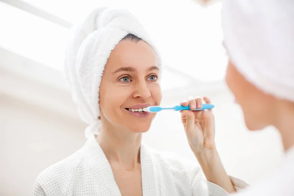 ハッピーレディブラッシング歯ブラシで中年女性立ちますバスルームで屋内で朝 — ストック写真