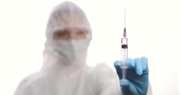 Doctor in a protective suit with a syringe looking to a syringe with vaccine. Blurred background. — Stock Video