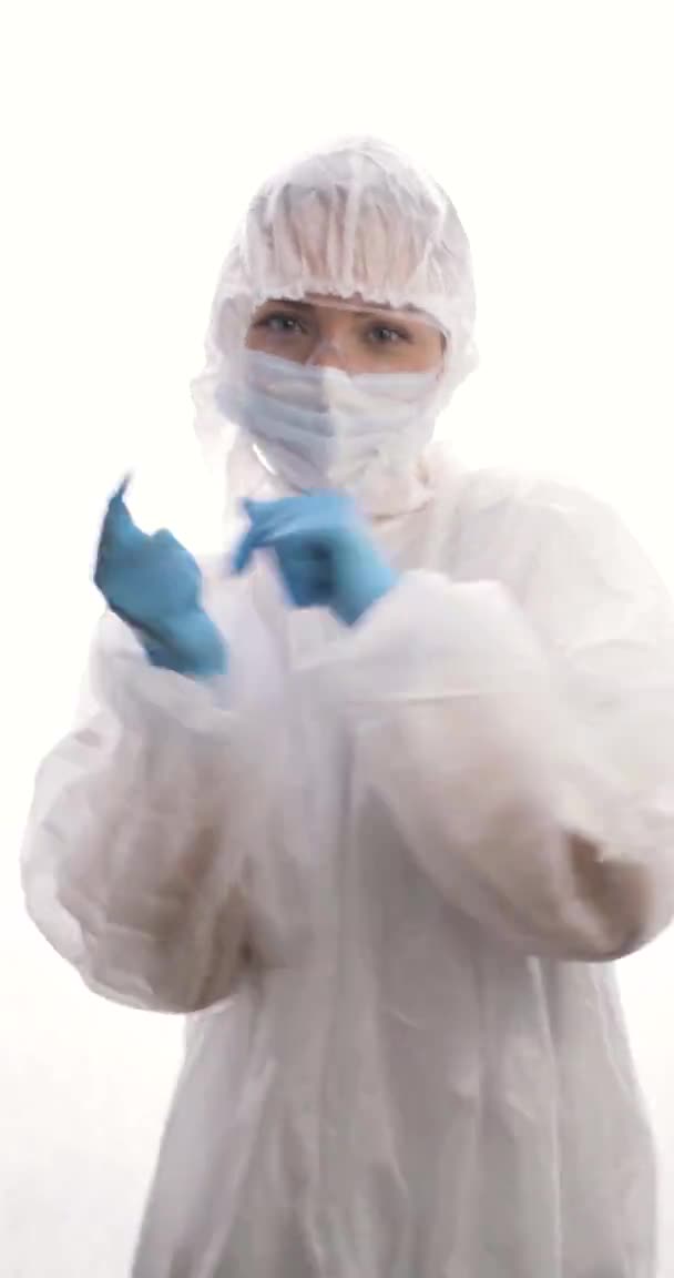 Ung kvinna i skyddskläder, mask och handskar dansar och dårar under pausen på en vit bakgrund. Vertikal video. — Stockvideo