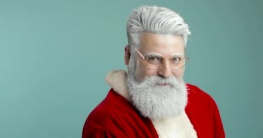 Noel Baba kıyafetli sakallı adam gülümseyen ve kameraya kar üfleyen, mavi arka planda izole edilmiş - noel konsepti yakın çekim