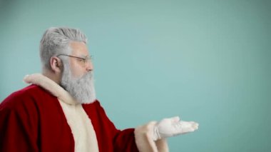 Noel Baba kıyafetli sakallı adam gülümseyen ve kameraya kar üfleyen, mavi arka planda izole edilmiş - noel konsepti yakın çekim
