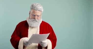 Hayal kırıklığına uğramış bir Noel Baba 'nın portresi kameraya bakıyor ve çocuklardan gelen mektupları okuyor. Öfkeli, hoşnutsuz, agresif, mavi arka planda Noel Baba.