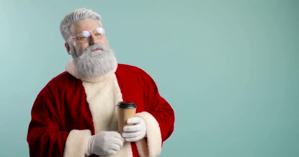 Trendiger, fröhlicher, fröhlicher Weihnachtsmann-Hipster mit einer Tasse Kaffee zum Mitnehmen. trinkt Kaffee und ist glücklich. Blauer Hintergrund — Stockvideo