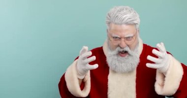 Kameraya bakan hayal kırıklığına uğramış bir Noel Baba portresi. Öfkeli, hoşnutsuz, agresif, mavi arka planda Noel Baba.