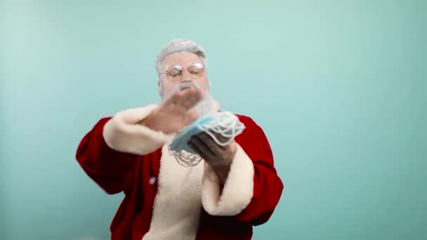 Lustige Weihnachtsmänner werfen pathetisch medizinische Schutzmasken in verschiedene Richtungen, blauer Hintergrund. Zeitlupe — Stockvideo