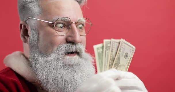 Snygg glad jultomte på en röd bakgrund poserar med pengar dollar. Ekonomi, pengar, sedlar. Närbild — Stockvideo