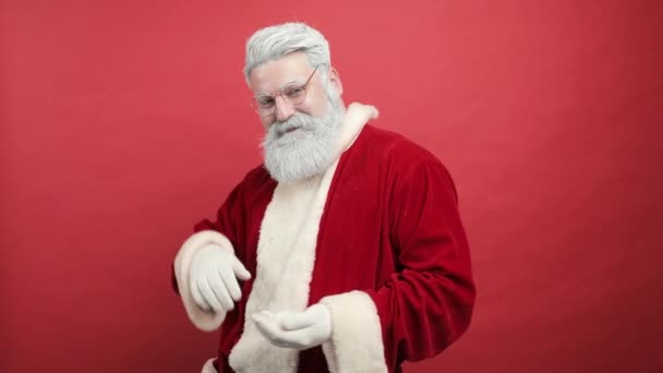 Slow motion stijlvolle, vrolijke, vrolijke, vrolijke baard man in Santa Claus kleding glimlachen en blazen sneeuw in de camera, geïsoleerd over rode achtergrond - kerst concept close-up — Stockvideo