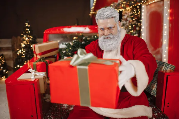 Porträtt av en snygg jultomte med en gåva i händerna, en hel del presenter på baksidan av en bil. Förbereda presenter för firandet av jul och nyår — Stockfoto
