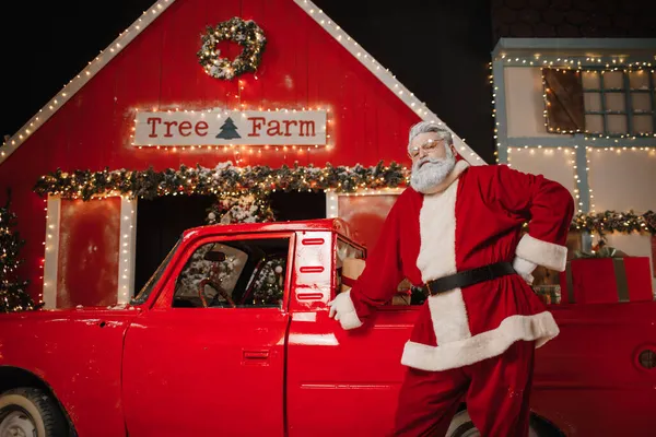 Πορτρέτο του ένα κομψό Santa Claus κοντά στο αυτοκίνητο με δώρα. Προετοιμασία δώρων για τον εορτασμό των Χριστουγέννων και της Πρωτοχρονιάς — Φωτογραφία Αρχείου
