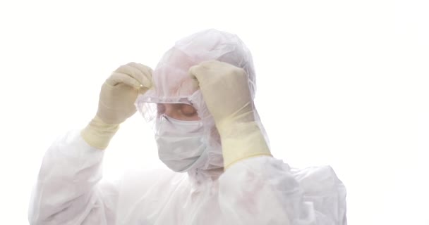 Porträtt av trött manlig läkare eller medicinsk personal som tar av huven på medicinska overaller, tar av skyddsglasögon, glovers och mask, ler efter att ha arbetat under en pandemi. — Stockvideo