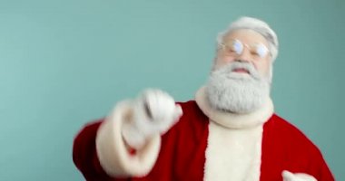 Modern Noel Baba 'nın portresi elini kameraya sallıyor, selamlıyor, insanları selamlıyor, çocukları selamlıyor. Noel 'le kutlar. Mavi arkaplan.